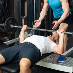 Man bench pressing in a gym with another man spotting.