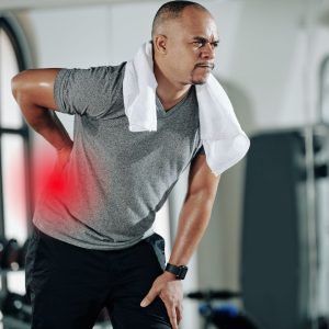 Middle-aged man in gym bent over in back pain.